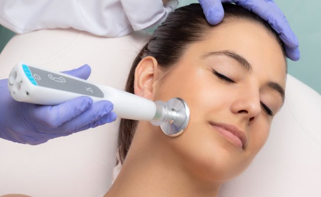 Close up of therapist doing facial mesotherapy treatment with flat head plasma pen. Electric impulse on woman's cheek stimulating new collagen.